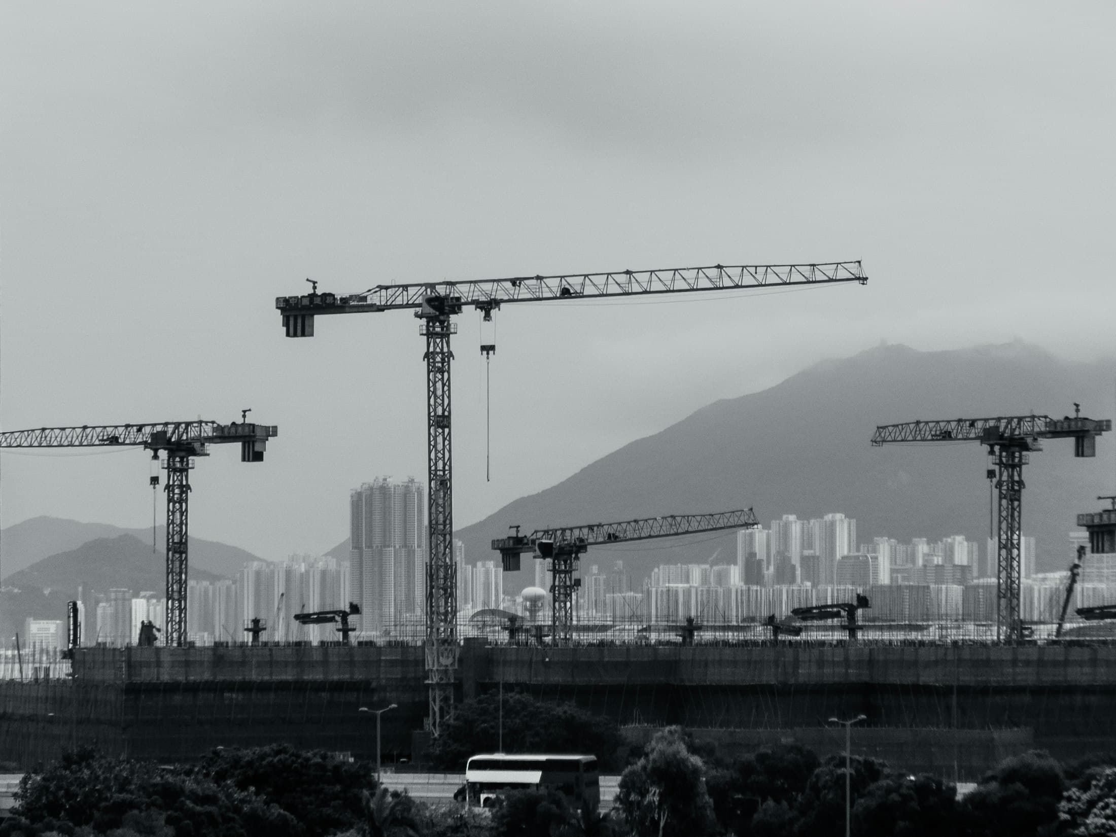 Tower cranes over a city skyline with mountains behind